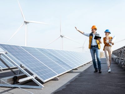 View on the rooftop solar power plant with two engineers walking and examining photovoltaic panels. Concept of alternative energy and its service